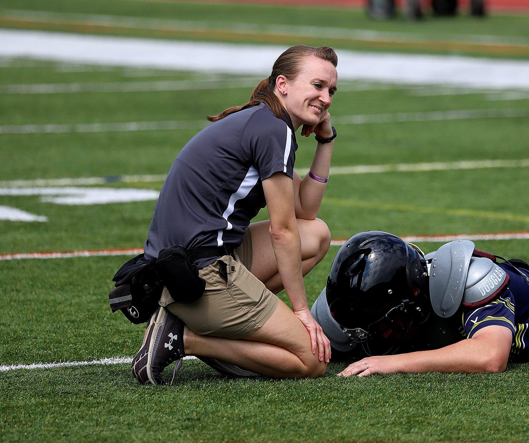 Liz Delehanty kneeling beside an athlete on a sports field.