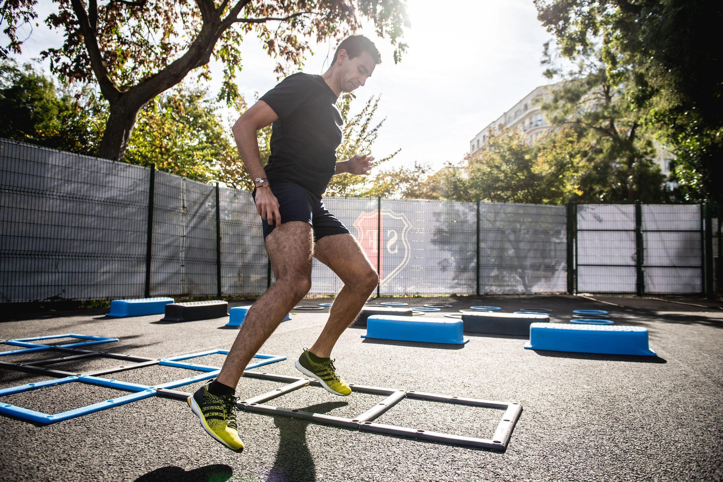An athlete stepping through an agility-ladder footwork drill on an outdoor training court.