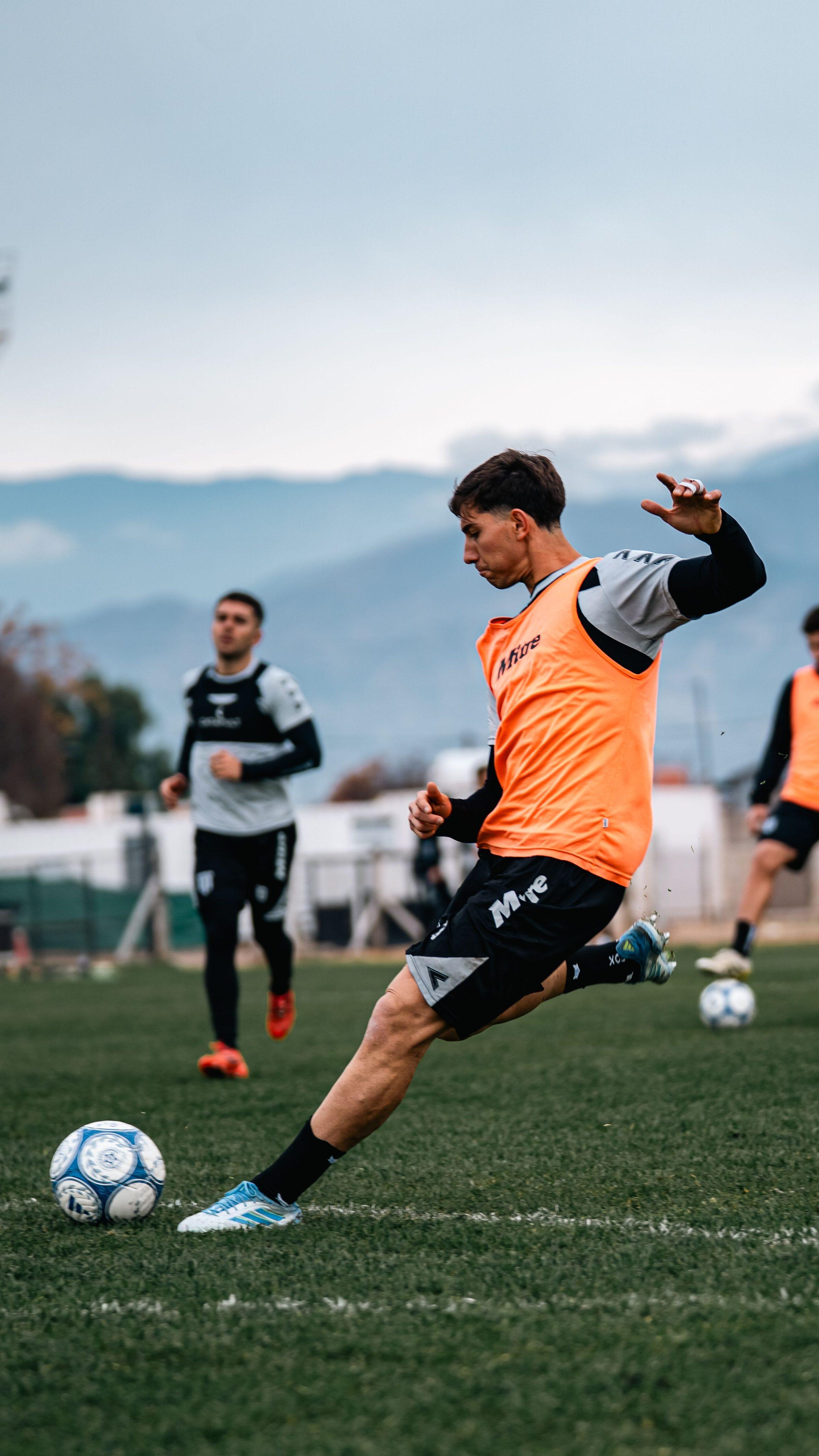 Young soccer players training on an outdoor grass field, with mountains in the distance.